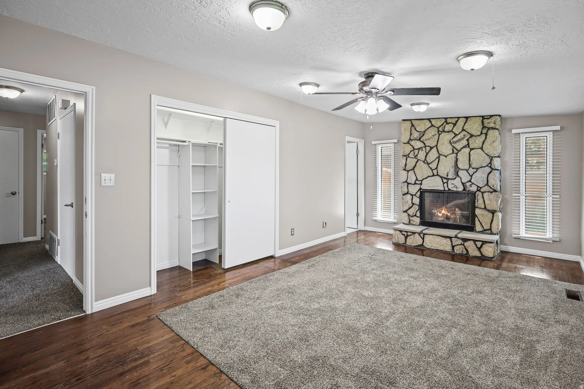 Feature stone-clad fireplace with hearth, wood-finish flooring, ceiling fan, recessed lighting, and built-in closet shelving