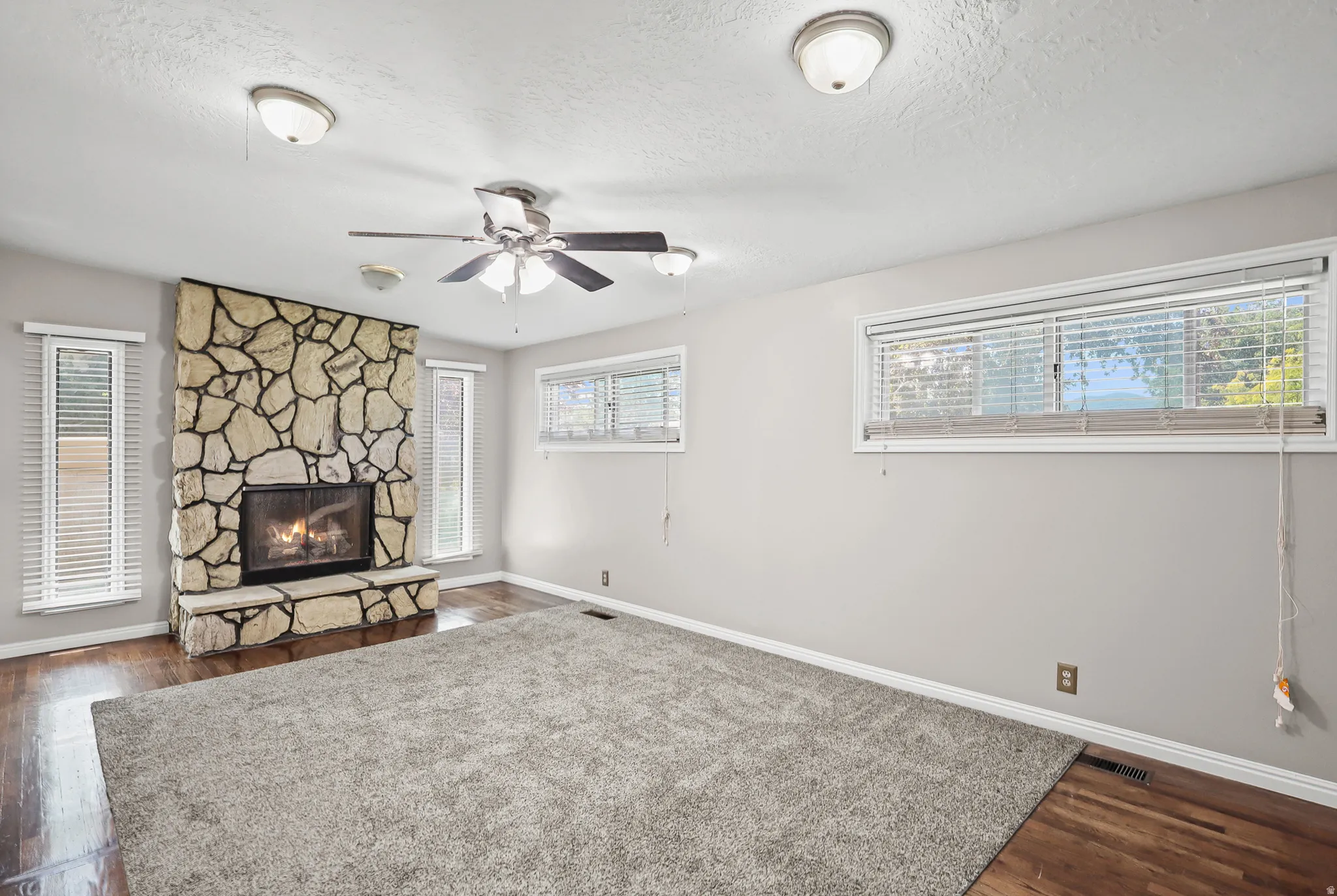 Stone fireplace with hearth, wood-finish flooring, and multiple windows