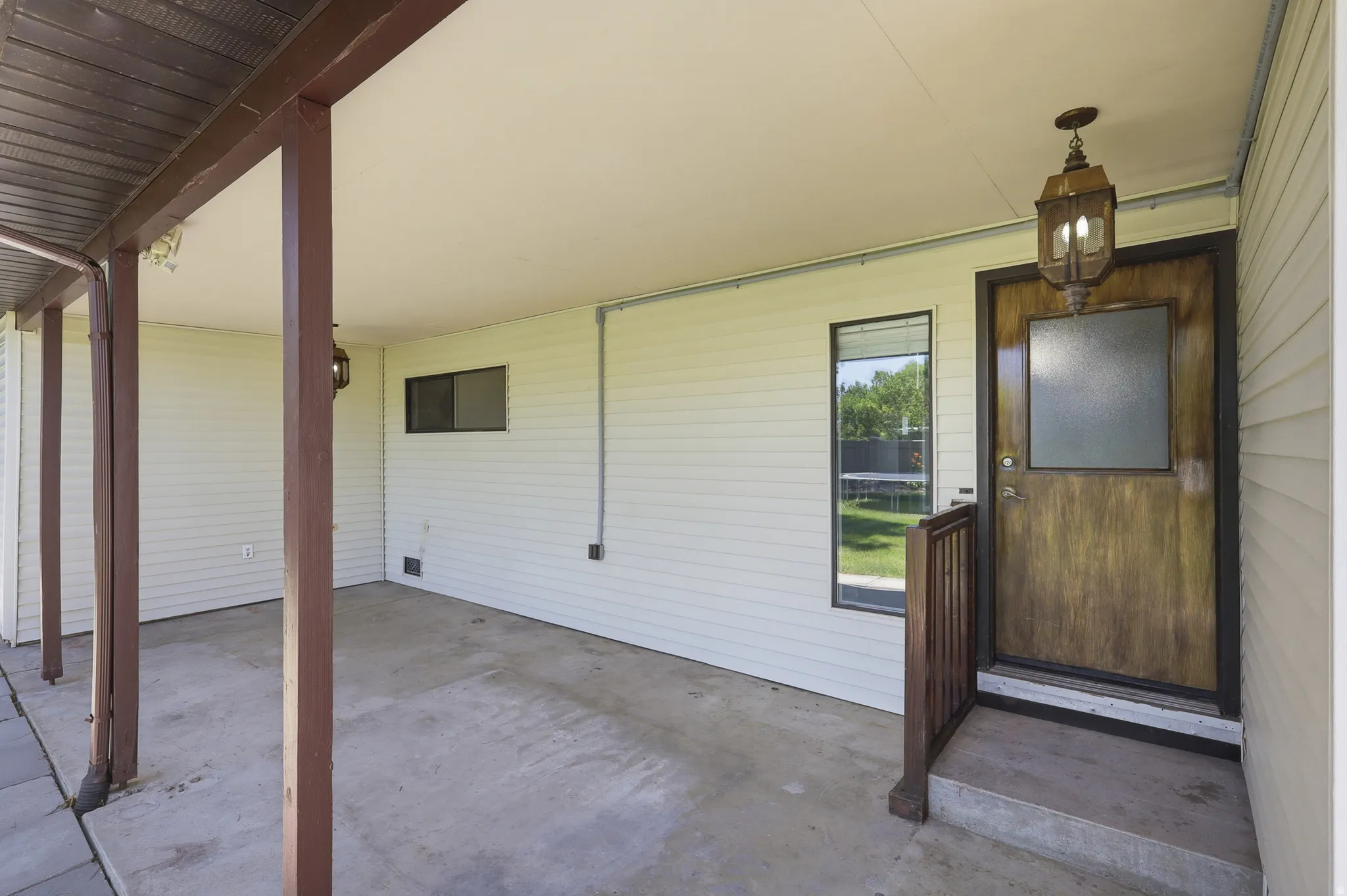 Covered entryway featuring a wood-finish door with frosted glass, an overhead lantern fixture, and white vinyl siding