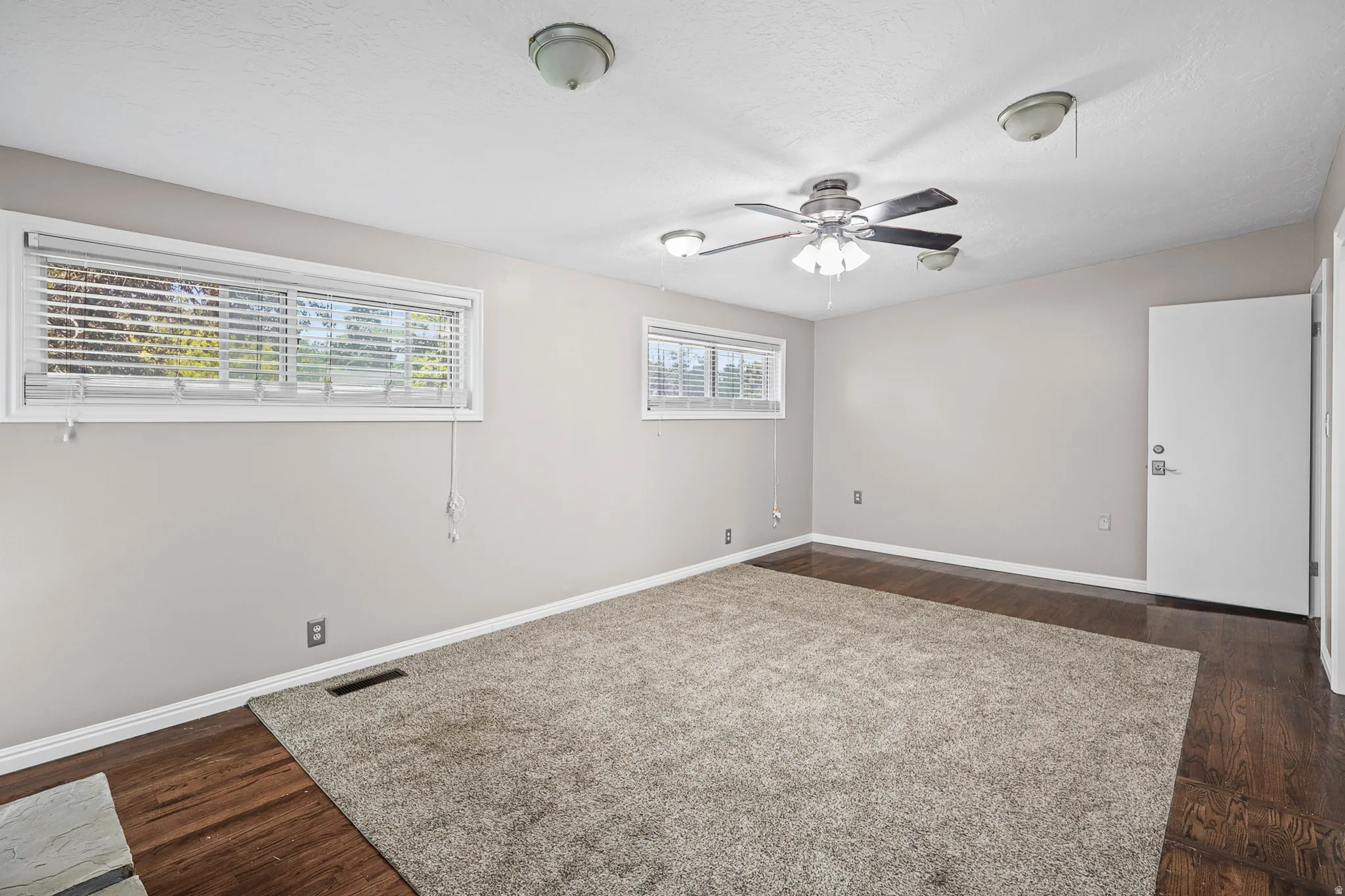Spacious room with wood-finish flooring partially covered by a large area rug, neutral wall paint, and white trim