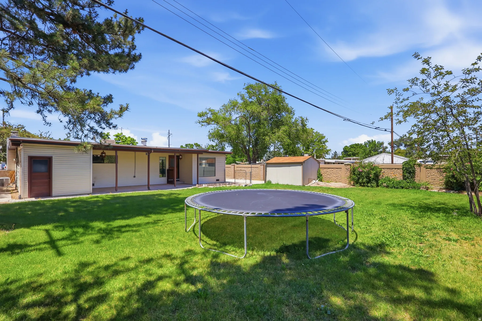 Spacious backyard featuring a substantial lawn, perimeter fencing, a covered patio, a storage shed, and mature trees
