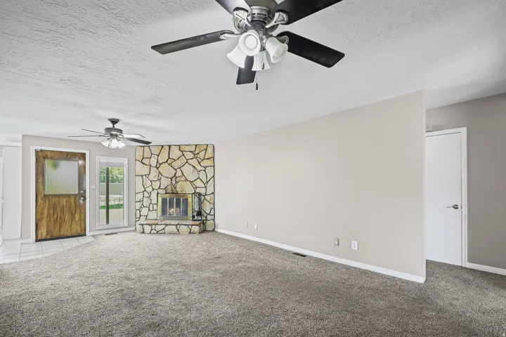 Spacious living area featuring a floor-to-ceiling stone fireplace surround, glass patio door, and wood-finish entry door with frosted glass panel