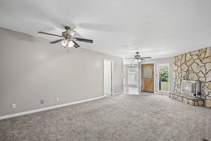 Spacious living area featuring neutral-toned walls, textured gray carpeting, and two ceiling fans with integrated lighting