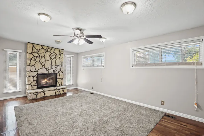 Stone fireplace with hearth, wood-finish flooring, and multiple windows