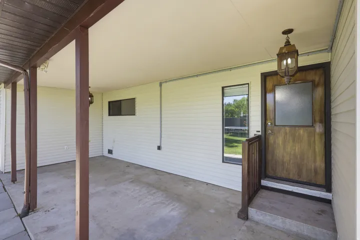 Covered entryway featuring a wood-finish door with frosted glass, an overhead lantern fixture, and white vinyl siding