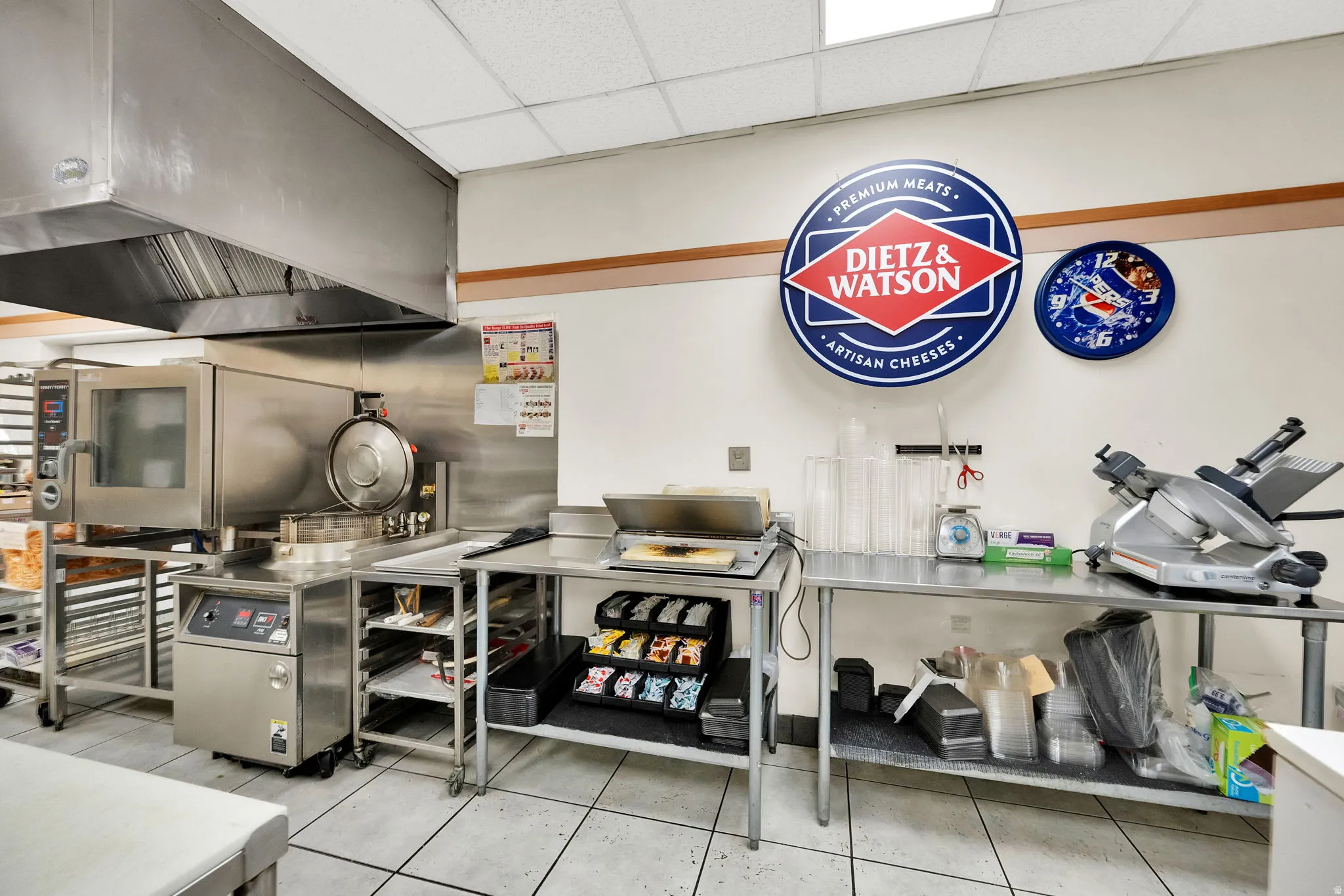 Commercial kitchen space featuring a large stainless steel range hood, commercial oven, and multiple stainless steel prep tables