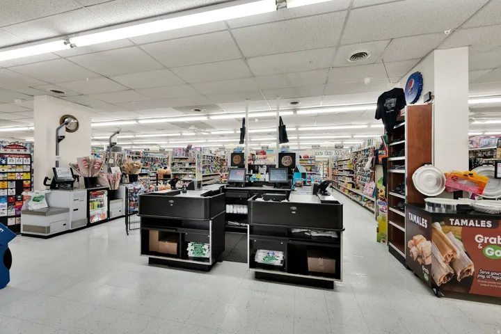 Commercial space featuring multiple checkout stations, integrated retail shelving, overhead fluorescent lighting, and white floor tiling