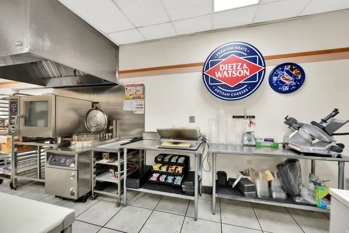 Commercial kitchen space featuring a large stainless steel range hood, commercial oven, and multiple stainless steel prep tables