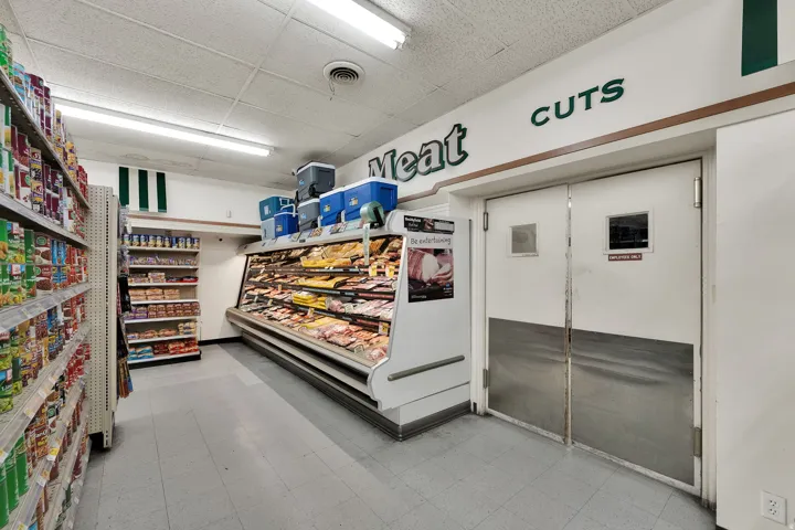 Commercial retail interior featuring a refrigerated display case, multiple shelving units, and a pair of industrial doors with kick plates