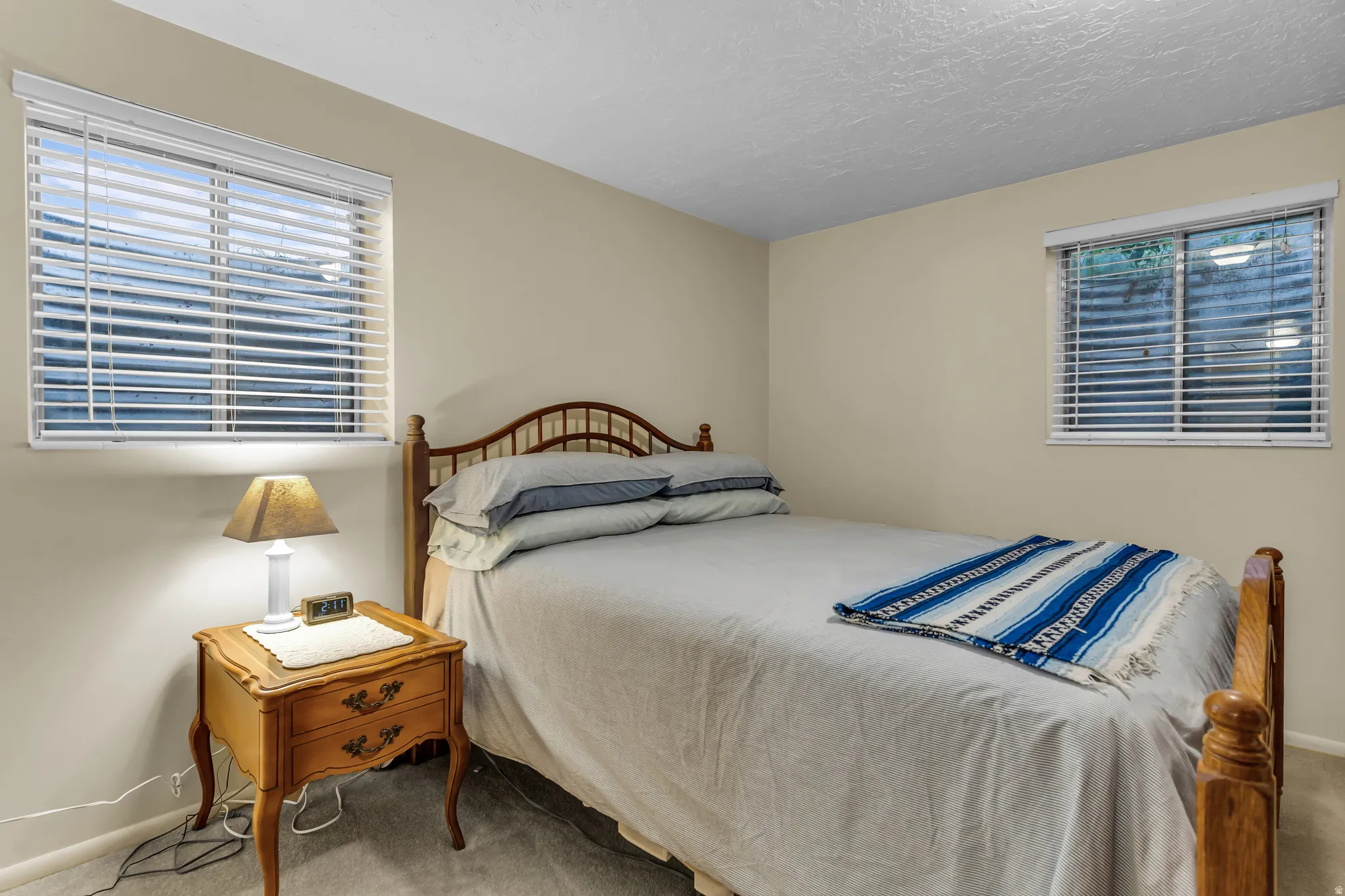Neutral wall paint and textured ceiling in this bedroom, featuring two windows with horizontal blinds
