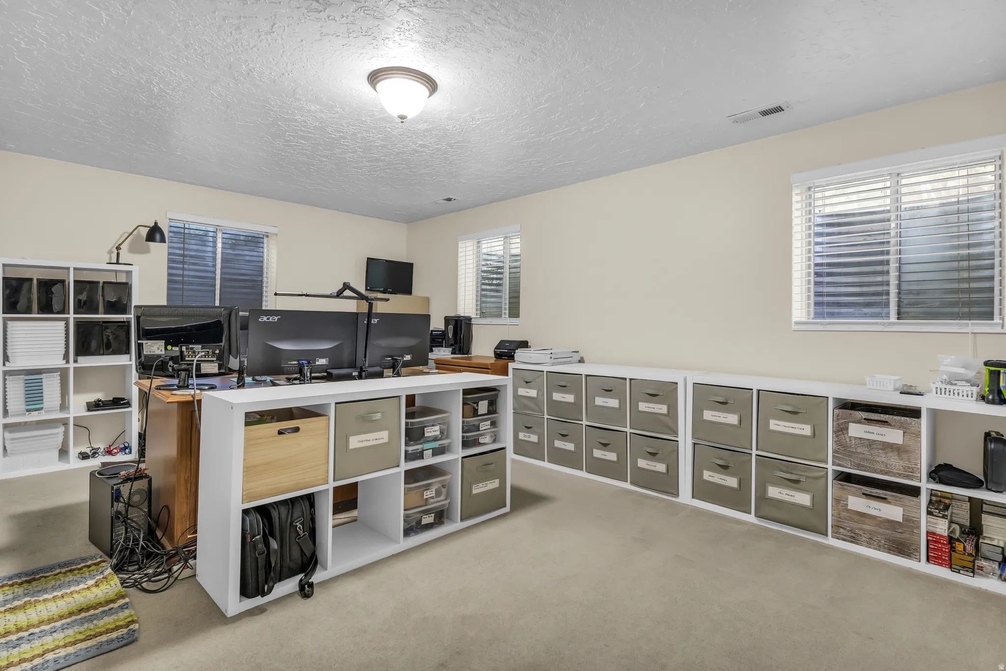 Spacious room featuring neutral carpeting, multiple windows with horizontal blinds, and a built-in shelving unit providing extensive storage