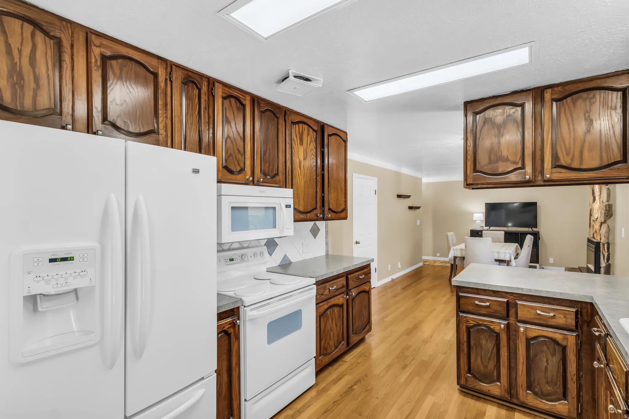 Kitchen featuring wood cabinetry, white appliances, light countertops, and wood-finish flooring