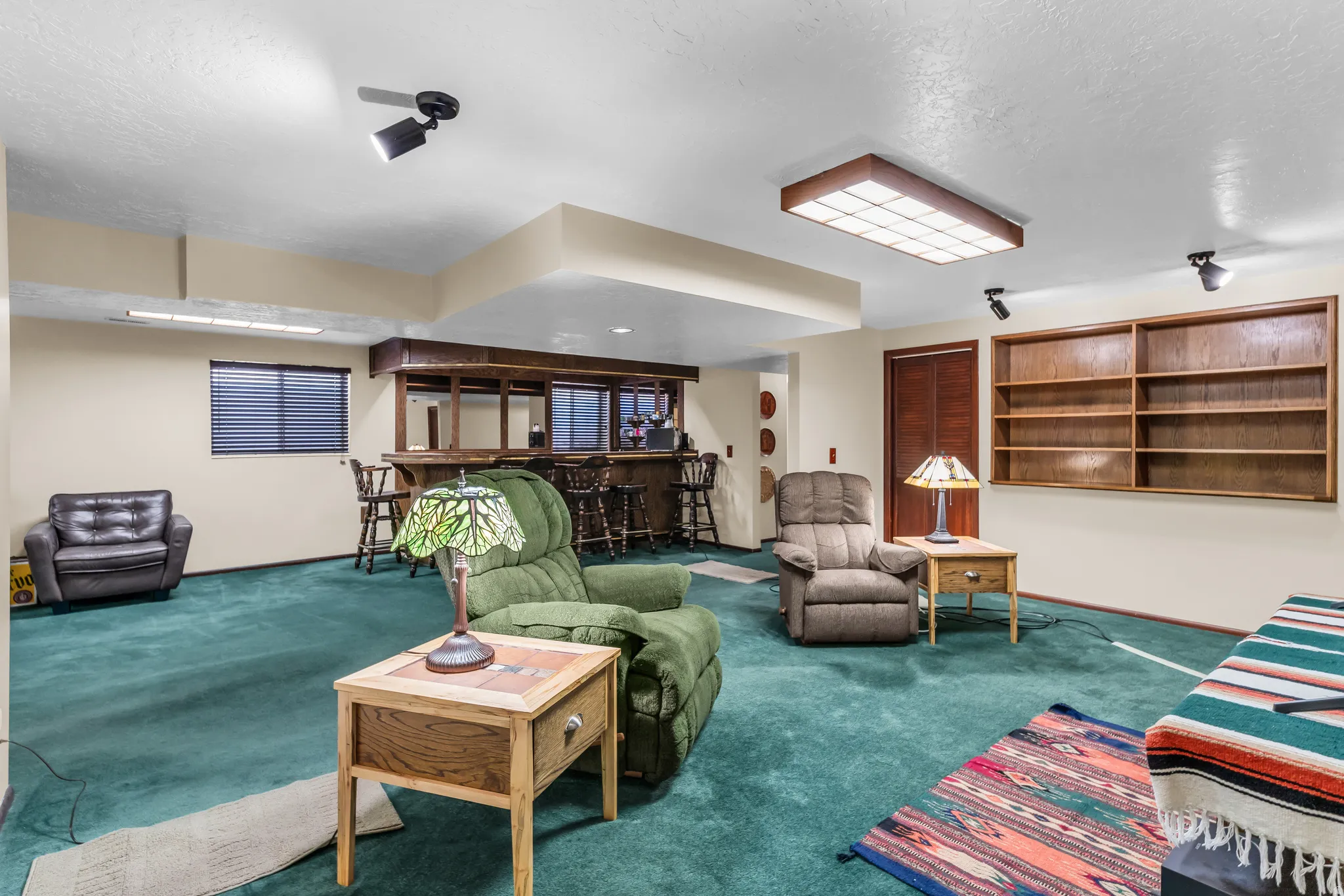 Recreation room featuring a built-in wet bar with wooden cabinetry, integrated shelving, and carpet flooring