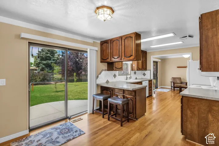 Kitchen featuring wood-finish flooring, rich wood cabinetry, light-toned countertops, and a tile backsplash