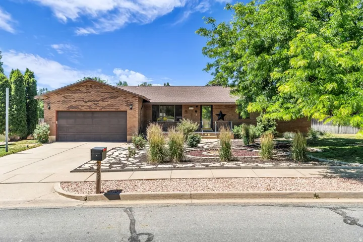 Brick exterior with an attached garage, featuring a paved driveway and mature landscaping with decorative stone beds