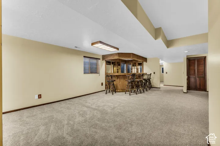 Spacious room featuring carpeting, a built-in wooden bar with seating, a window with blinds, and wooden bi-fold doors