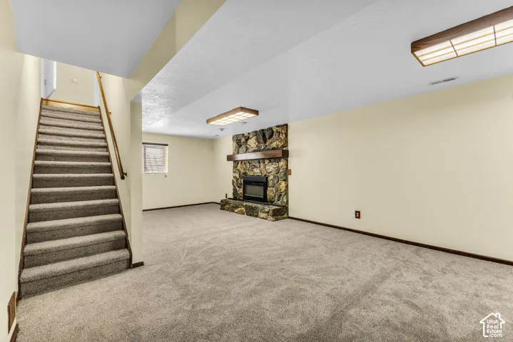 Spacious room with plush carpet, stone-clad fireplace with wood mantel, and wood-framed ceiling lighting