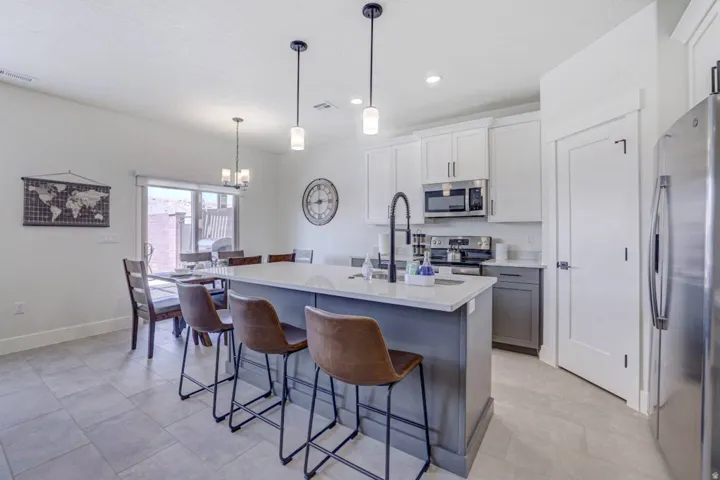 Kitchen featuring an island with pendant lighting, stainless steel appliances, white cabinetry, and light-toned tile flooring