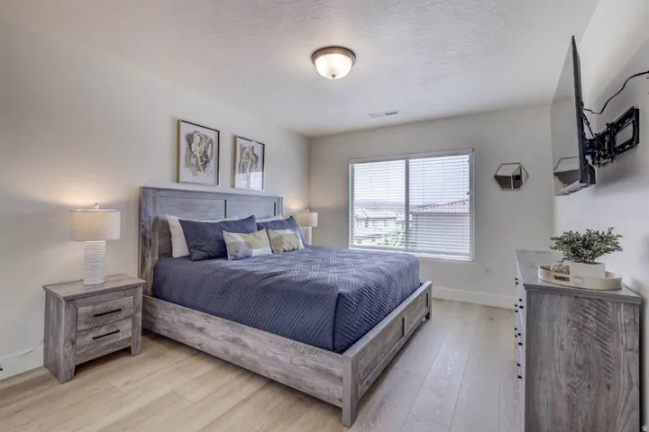 Spacious room with wood-finish flooring, a large window with blinds, and white walls