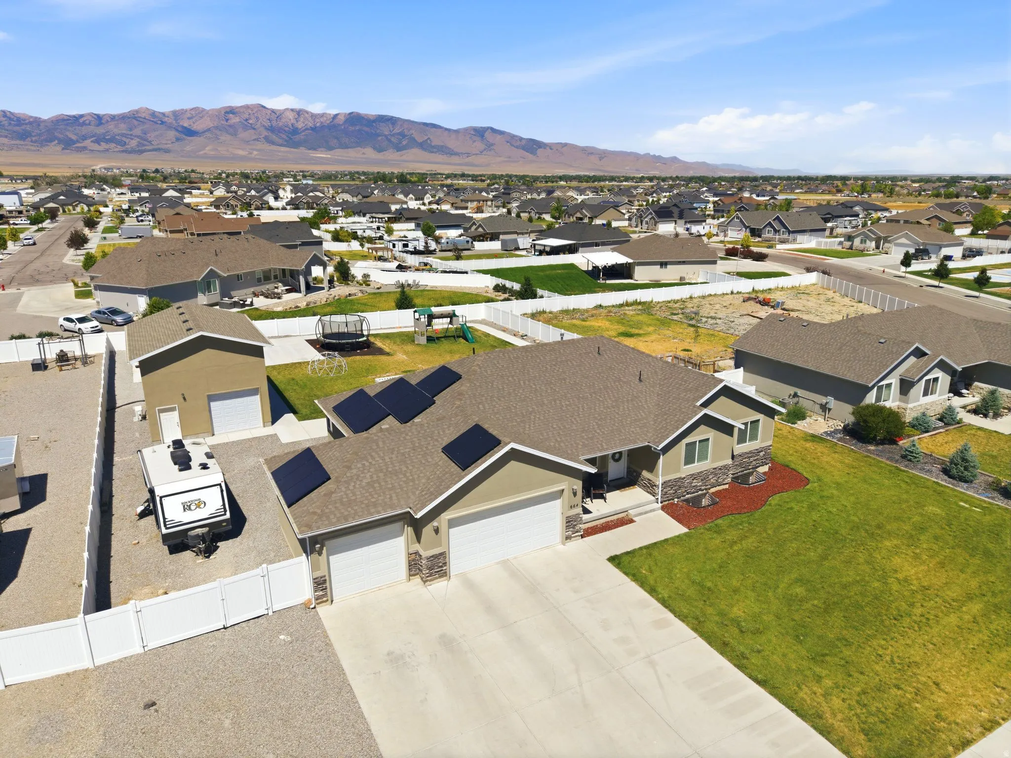 Single-story residence featuring a two-car garage, an additional detached single-car garage, and a gravel-paved side yard with white vinyl fencing