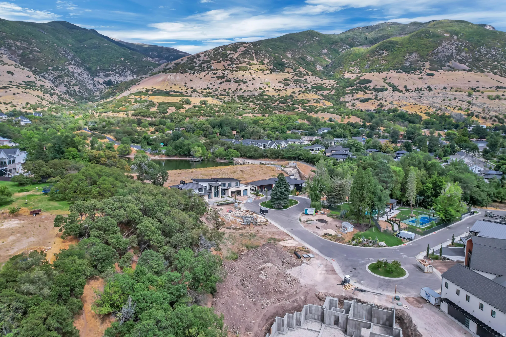 Residential development situated at the base of verdant mountains, featuring a pond and established trees