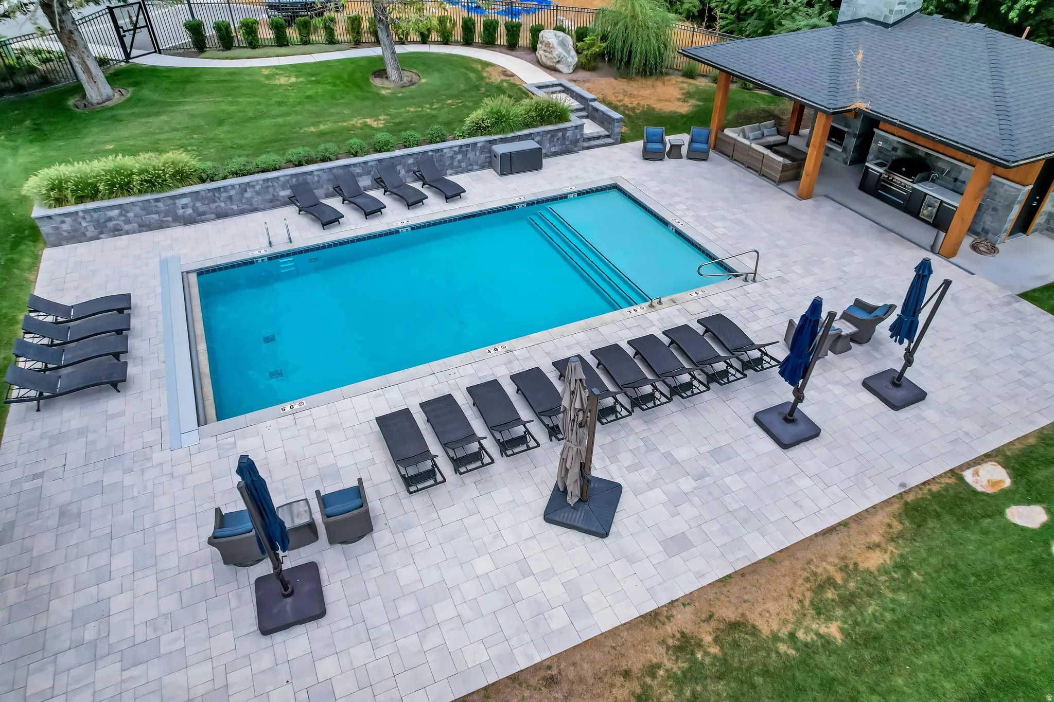 Outdoor swimming pool featuring a paver patio surround, built-in steps, and an adjacent covered outdoor kitchen with a stone facade