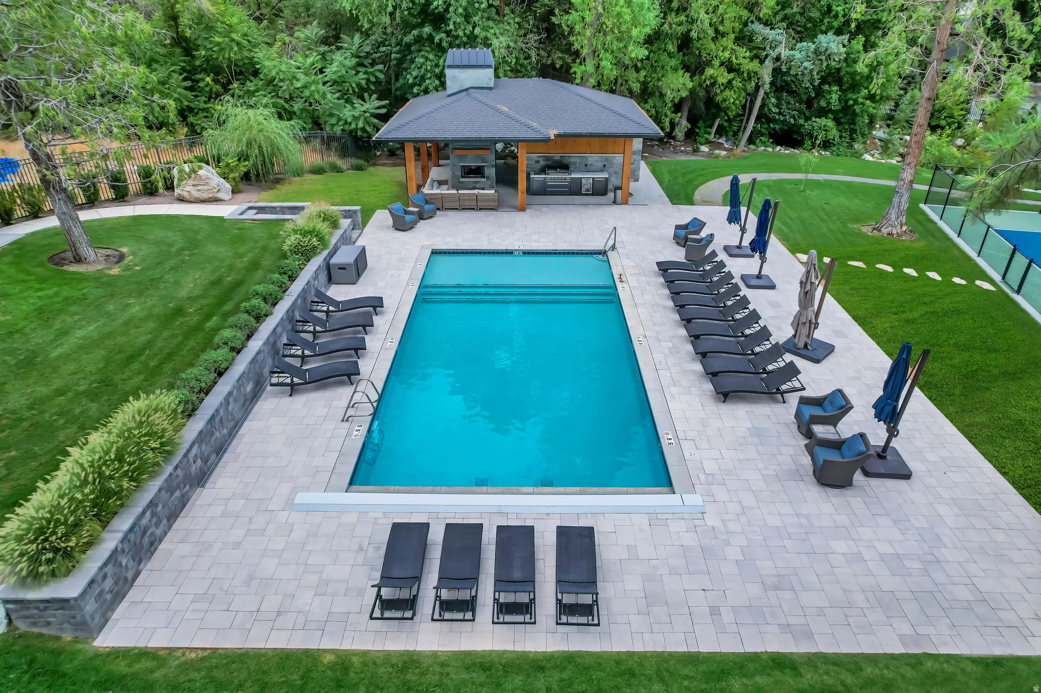Expansive outdoor living area featuring a rectangular swimming pool, paver patio, and a covered pavilion with a built-in outdoor kitchen and fireplace