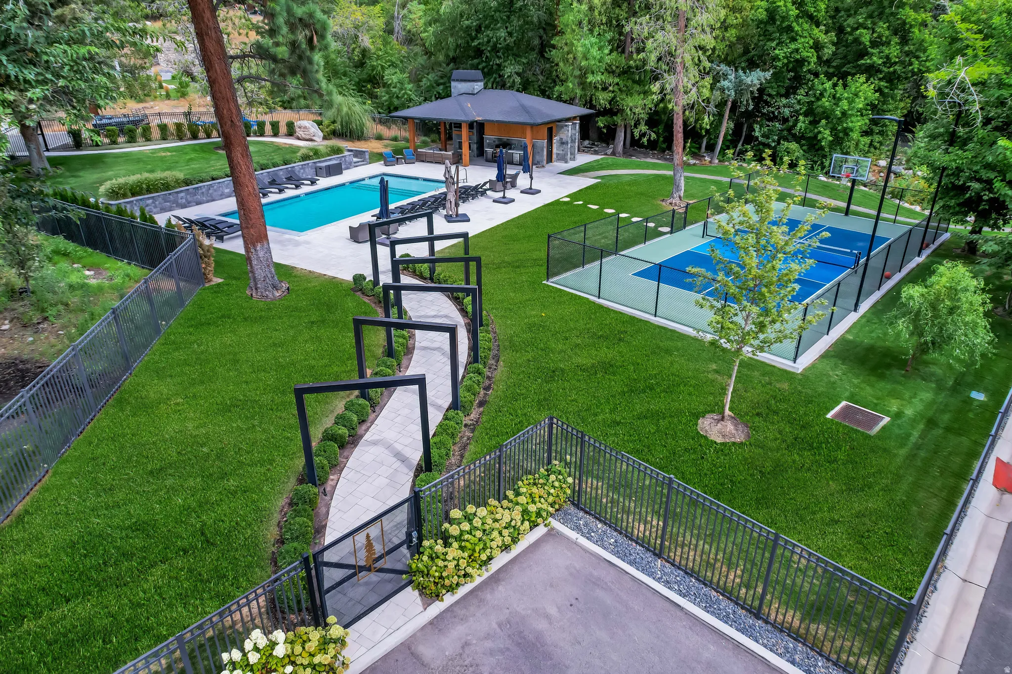 Expansive outdoor recreation area featuring a full-size swimming pool, a dedicated sports court, and a poolside pavilion with built-in bar