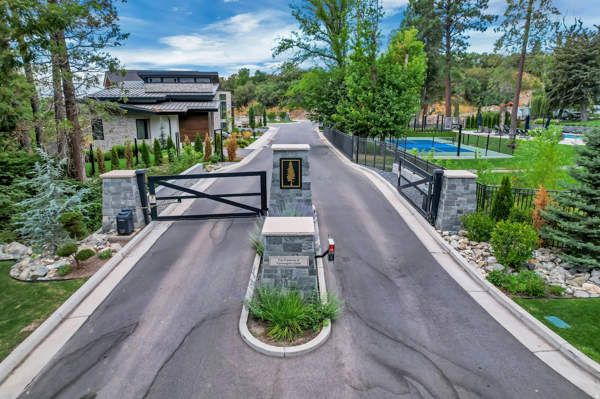 Stone pillar entryway with a black metal gate and an asphalt driveway