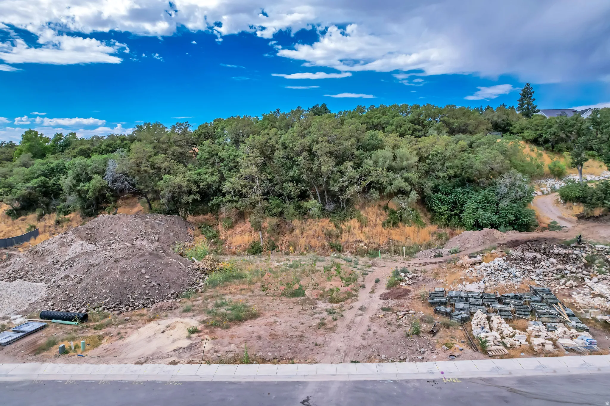 Building site featuring a paved road, concrete sidewalk, and graded lot
