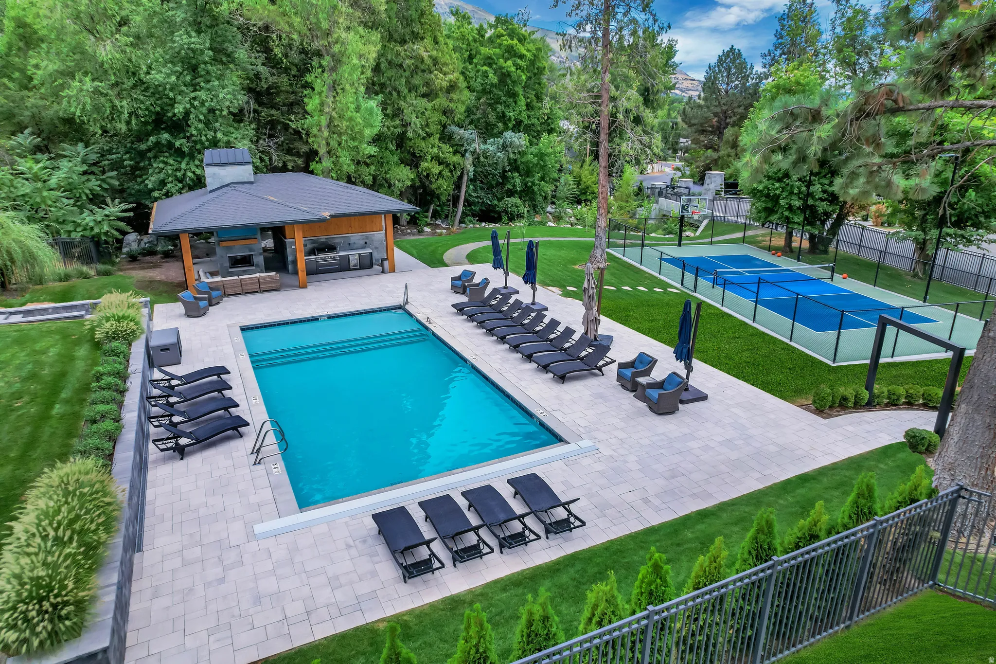 Expansive outdoor area featuring a rectangular swimming pool, paver patio, and a dedicated sport court
