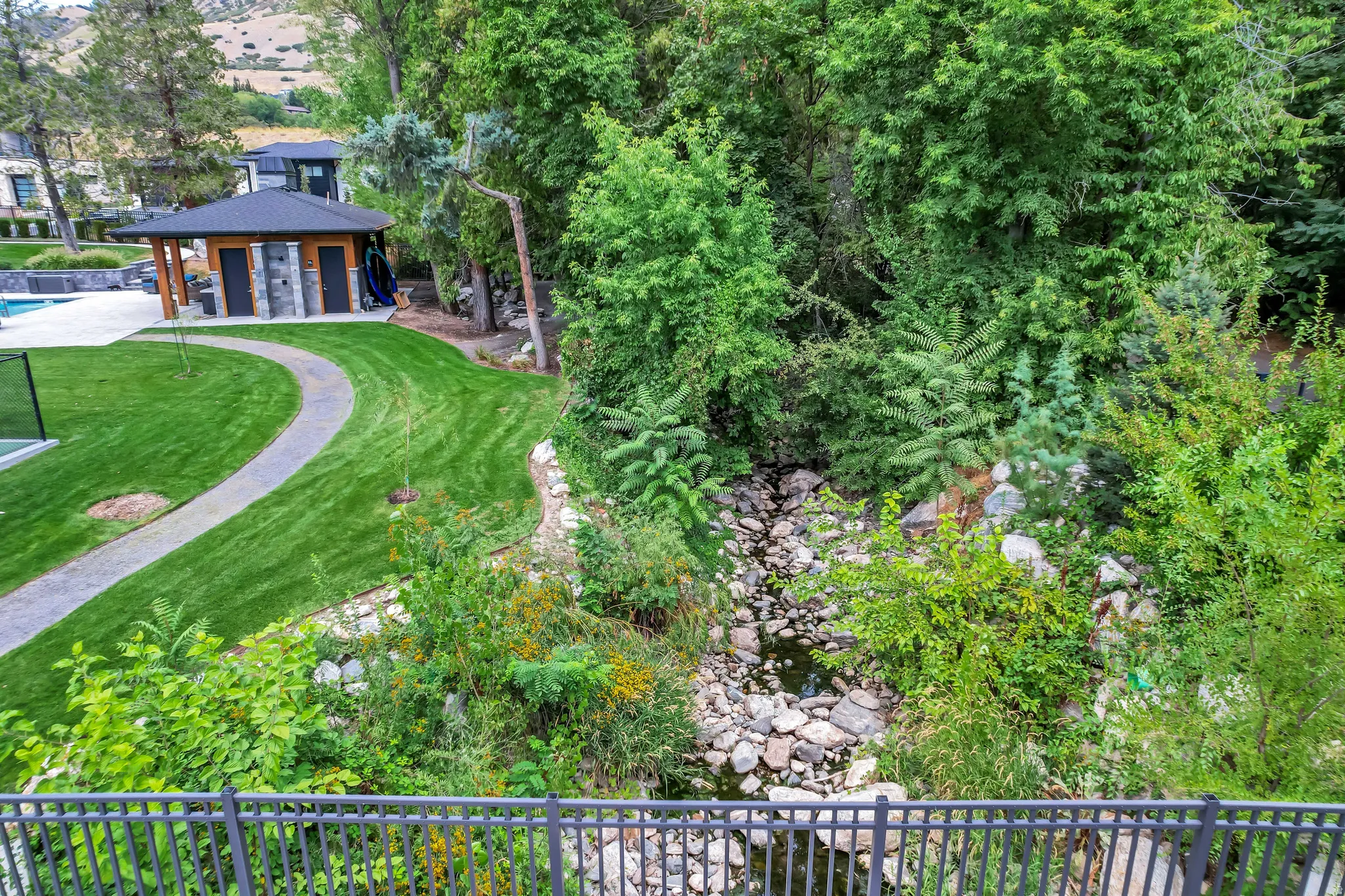 Manicured lawn with a stone pathway leading to a pool house featuring stone accents and a dark roof