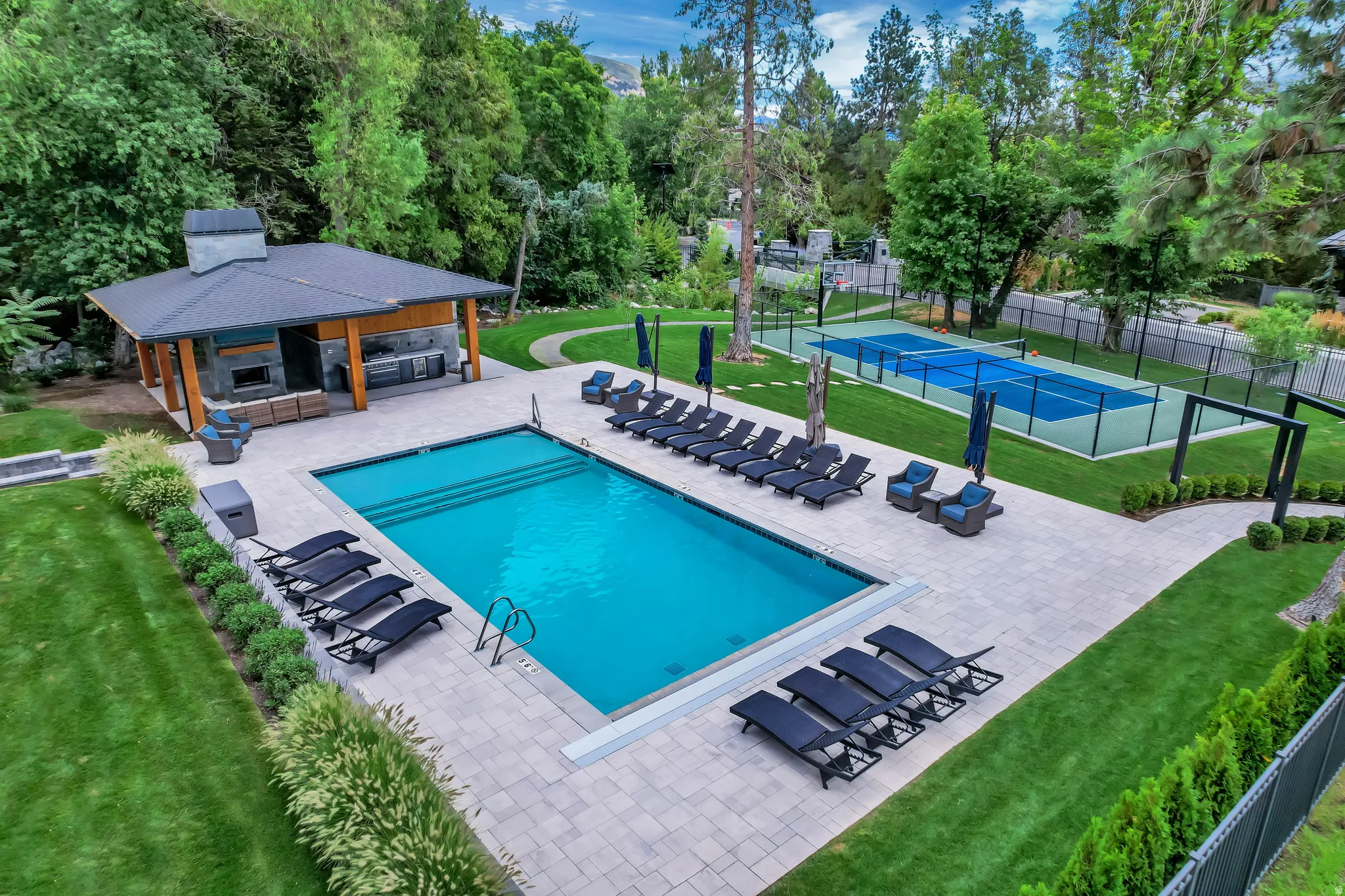 Expansive outdoor recreational area featuring a rectangular swimming pool, stone paver patio, and a dedicated paddle/pickleball court