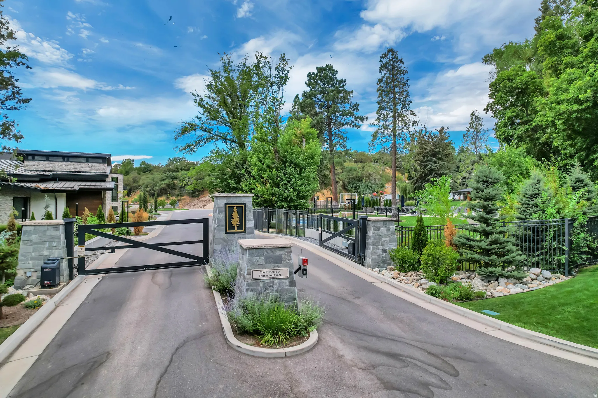 Gated entrance featuring stone pillars, black metal gates, and lush surrounding landscaping