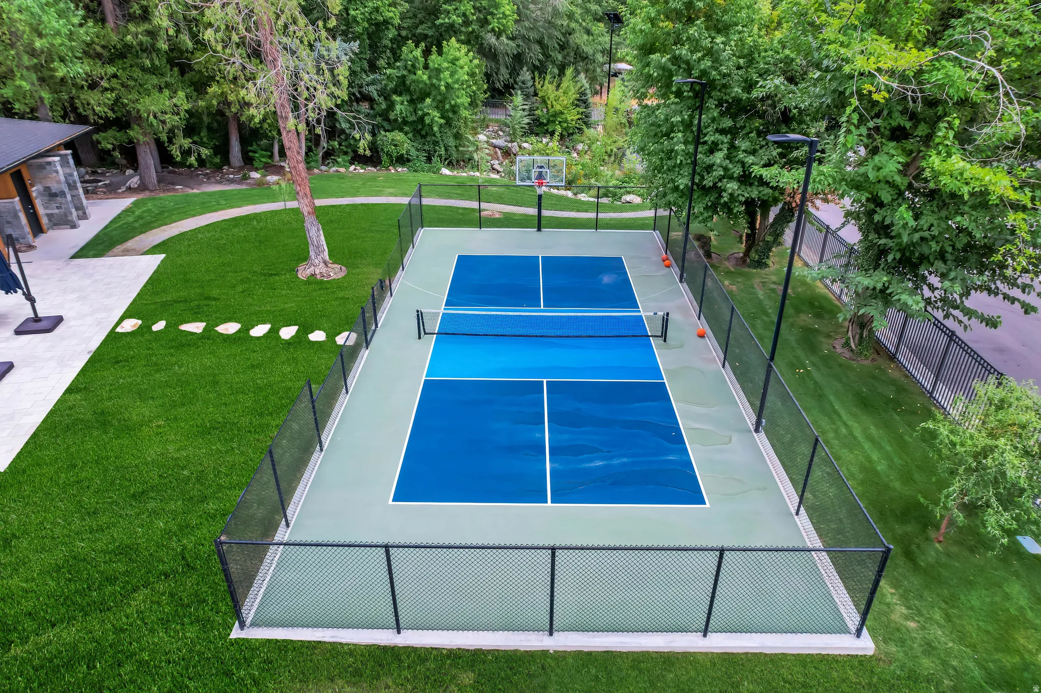 Outdoor sports court featuring blue and light green surfaces, perimeter fencing, and integrated basketball hoop