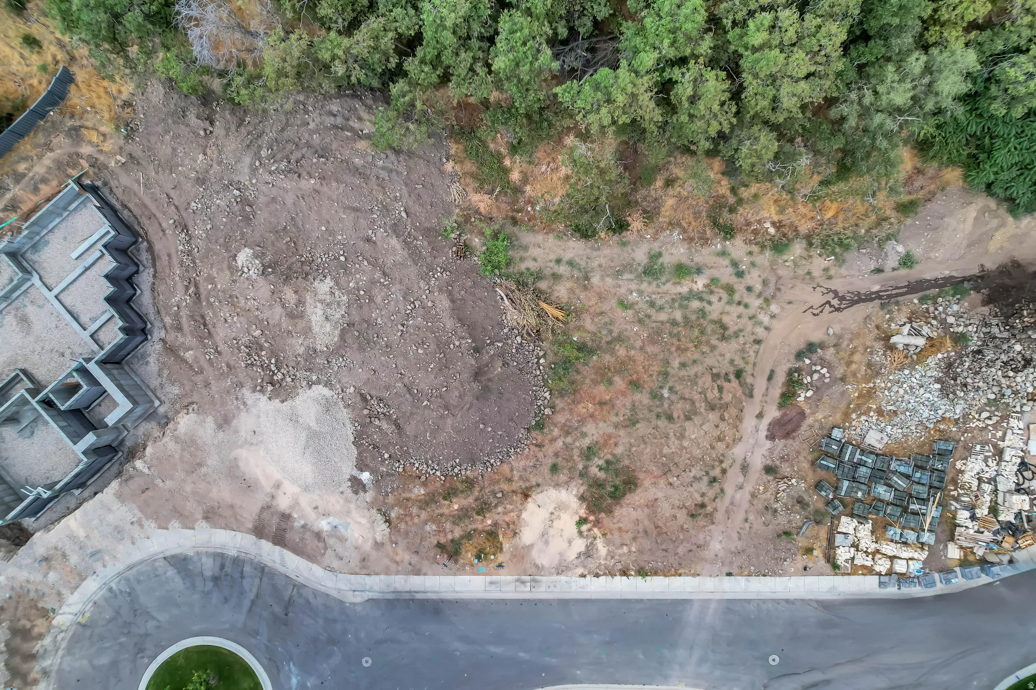 Expansive undeveloped lot featuring a partially constructed building foundation and substantial green space with mature trees