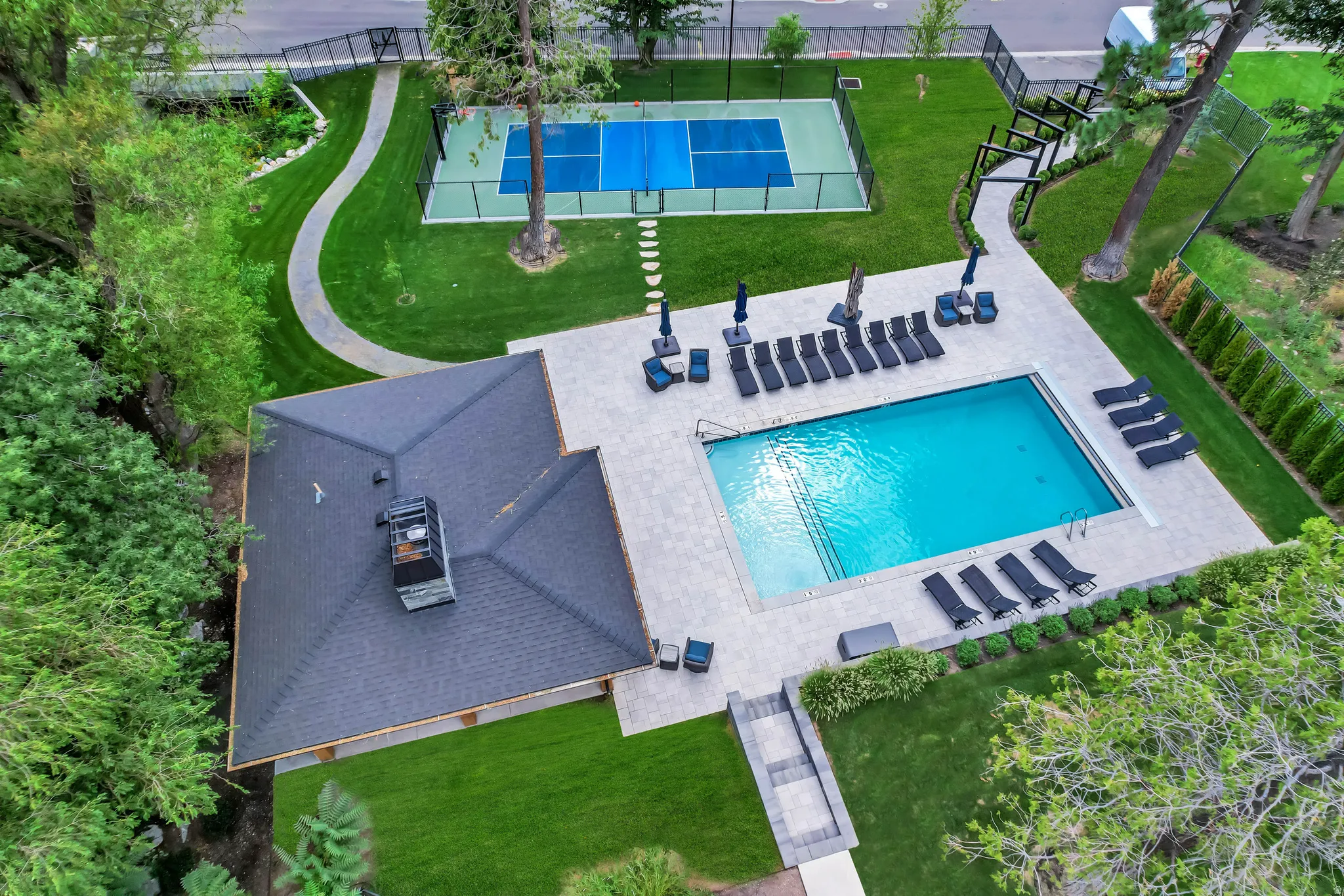 Outdoor recreational area featuring a rectangular swimming pool, an adjacent paved patio, and a separate fenced sports court