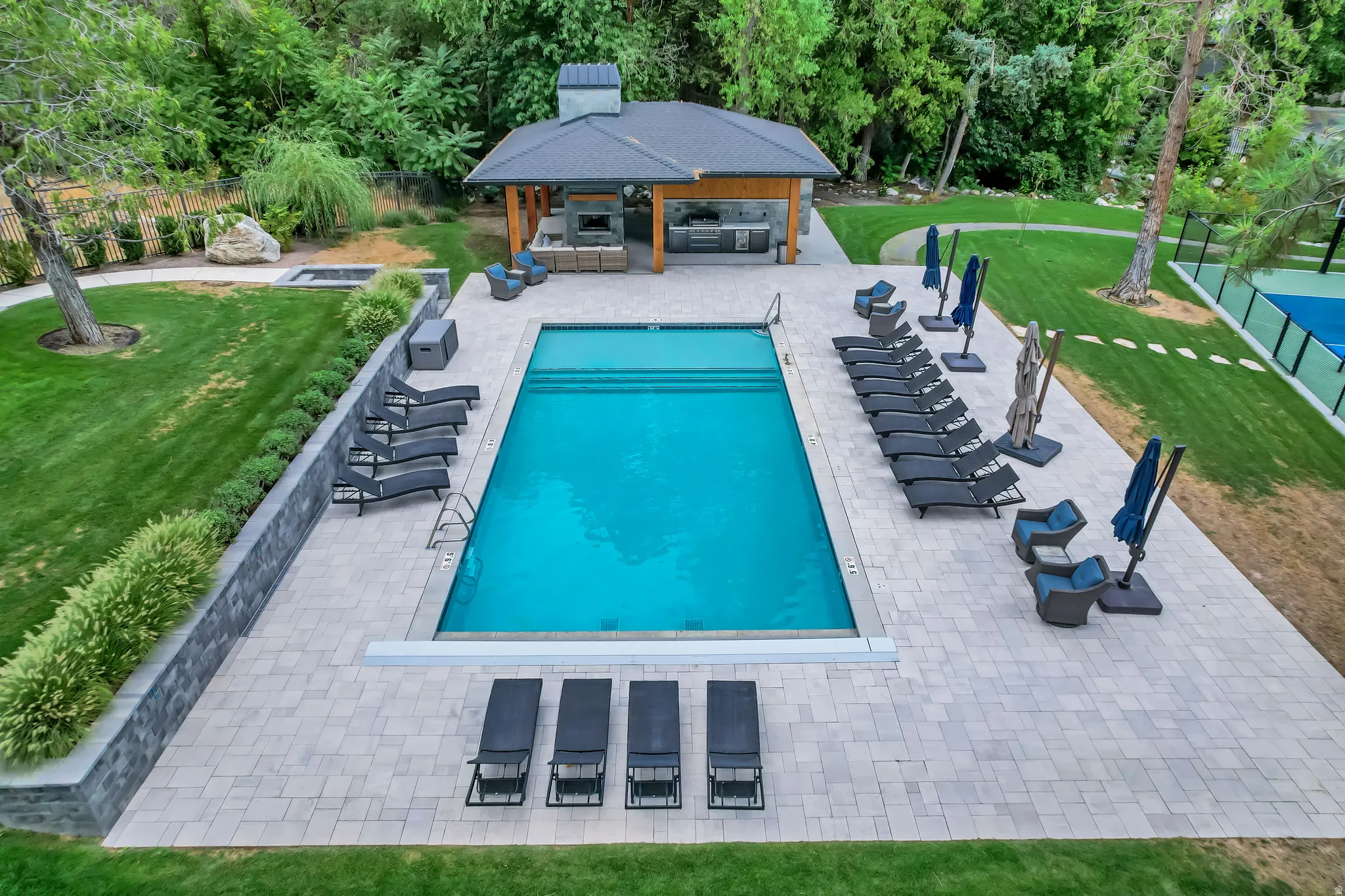 Expansive outdoor oasis featuring a large swimming pool, paver patio, and integrated pool house with an outdoor kitchen and fireplace