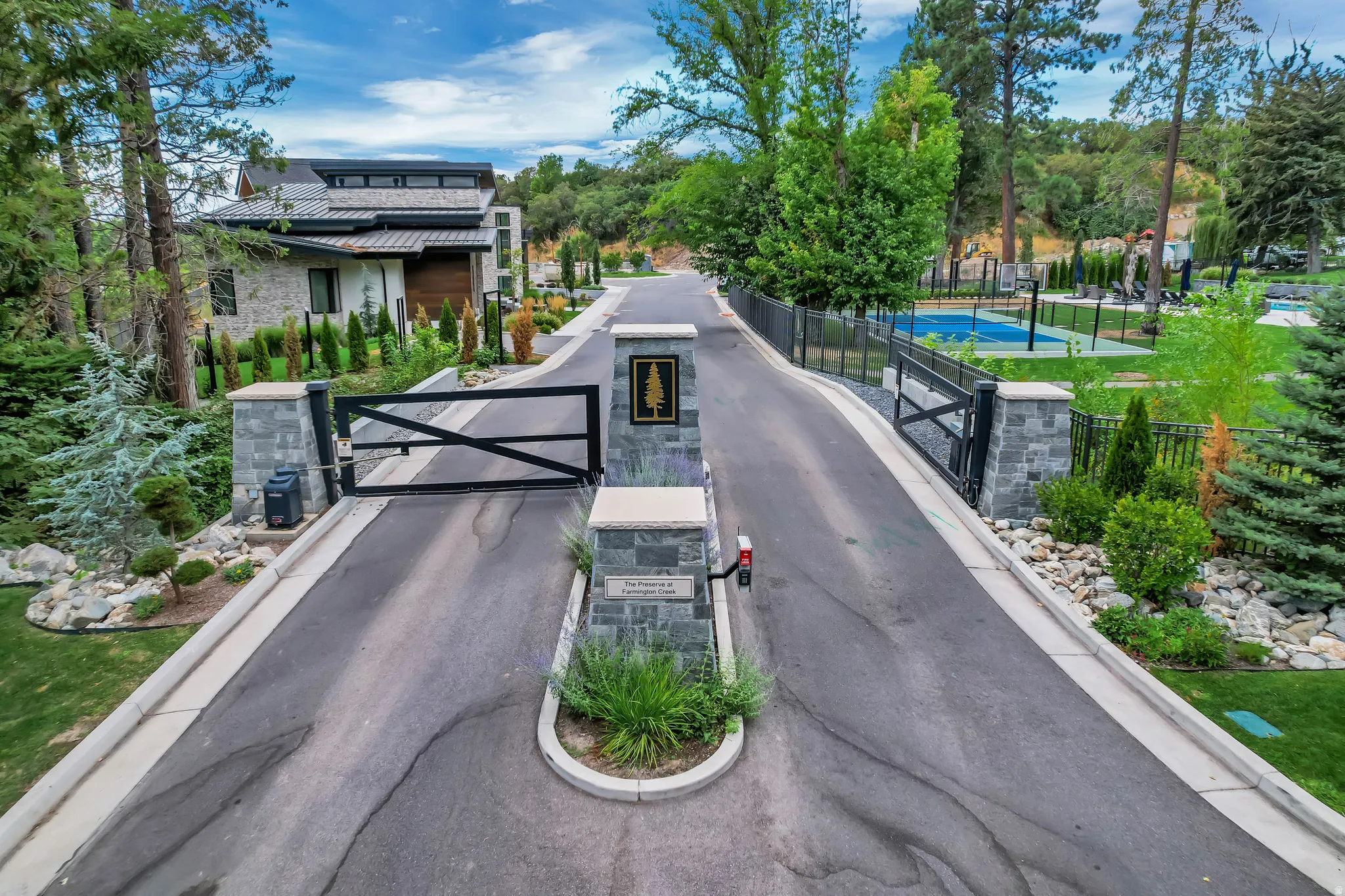Gated entry featuring stone-clad pillars, a dark metal gate, and surrounding landscaping