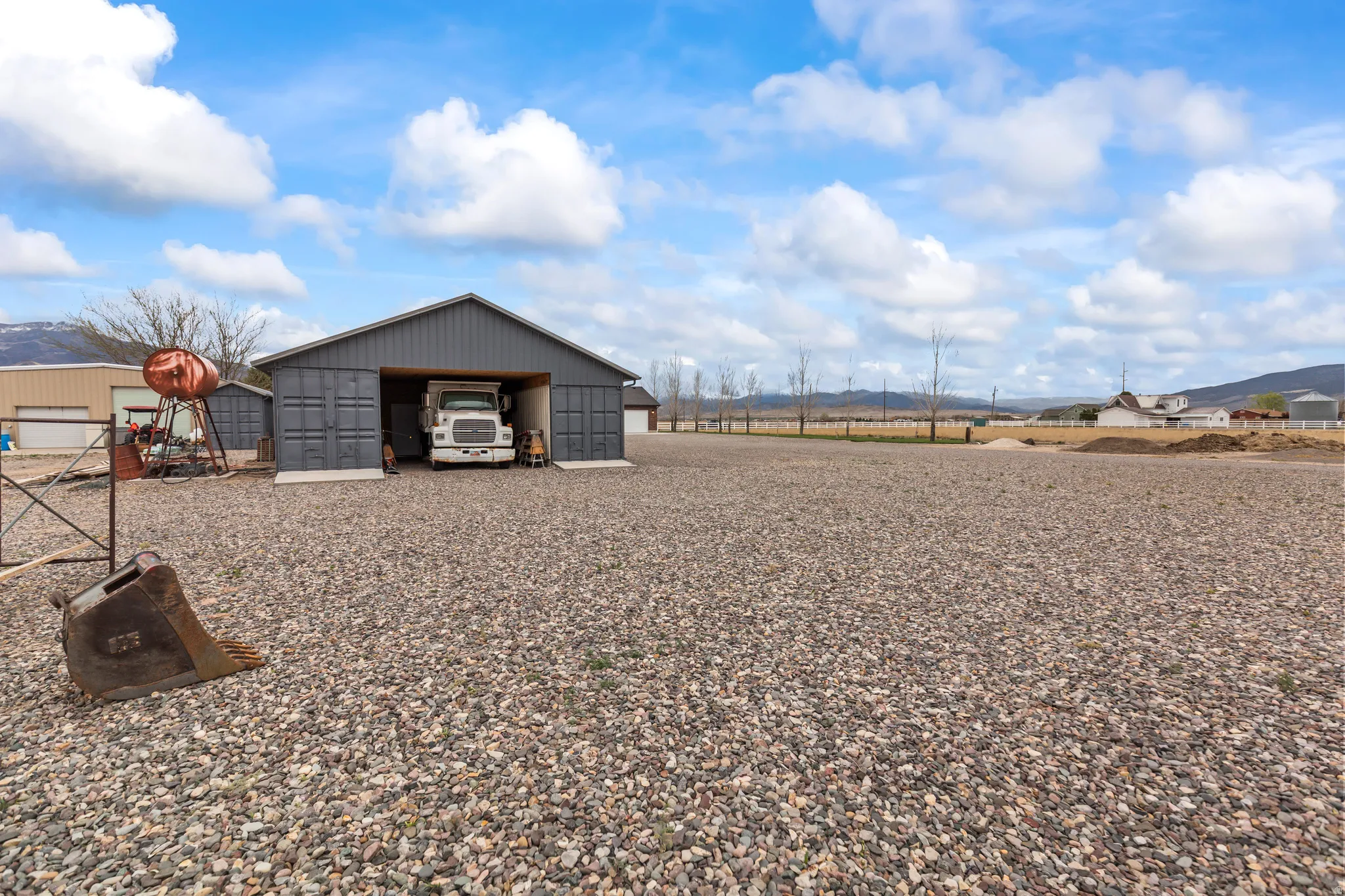 Spacious gravel lot with a large gray metal-sided utility building featuring multiple bay doors and an open bay