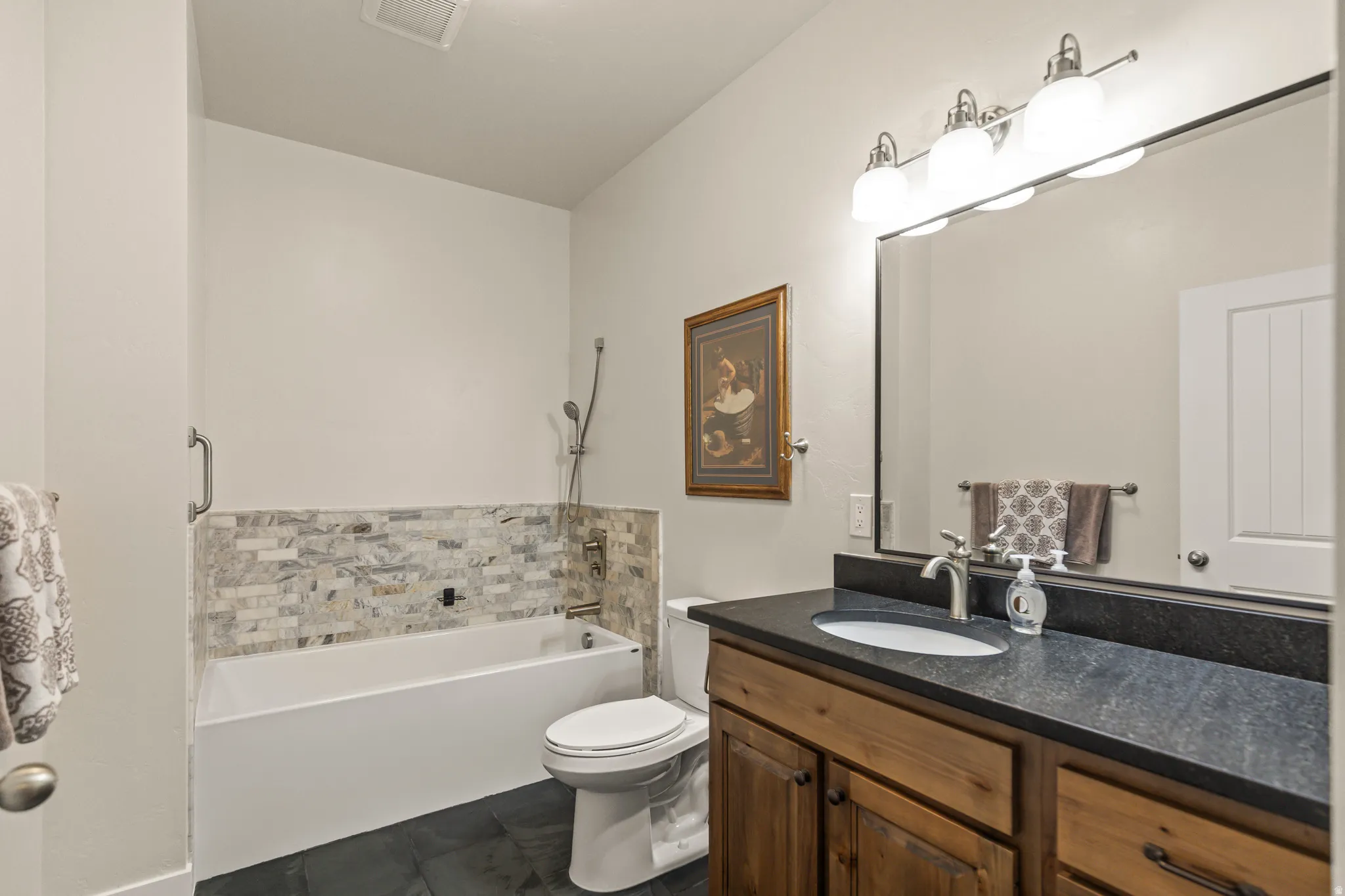 Bathroom featuring a full vanity with an undermount sink, dark countertop, and wood-finish cabinetry