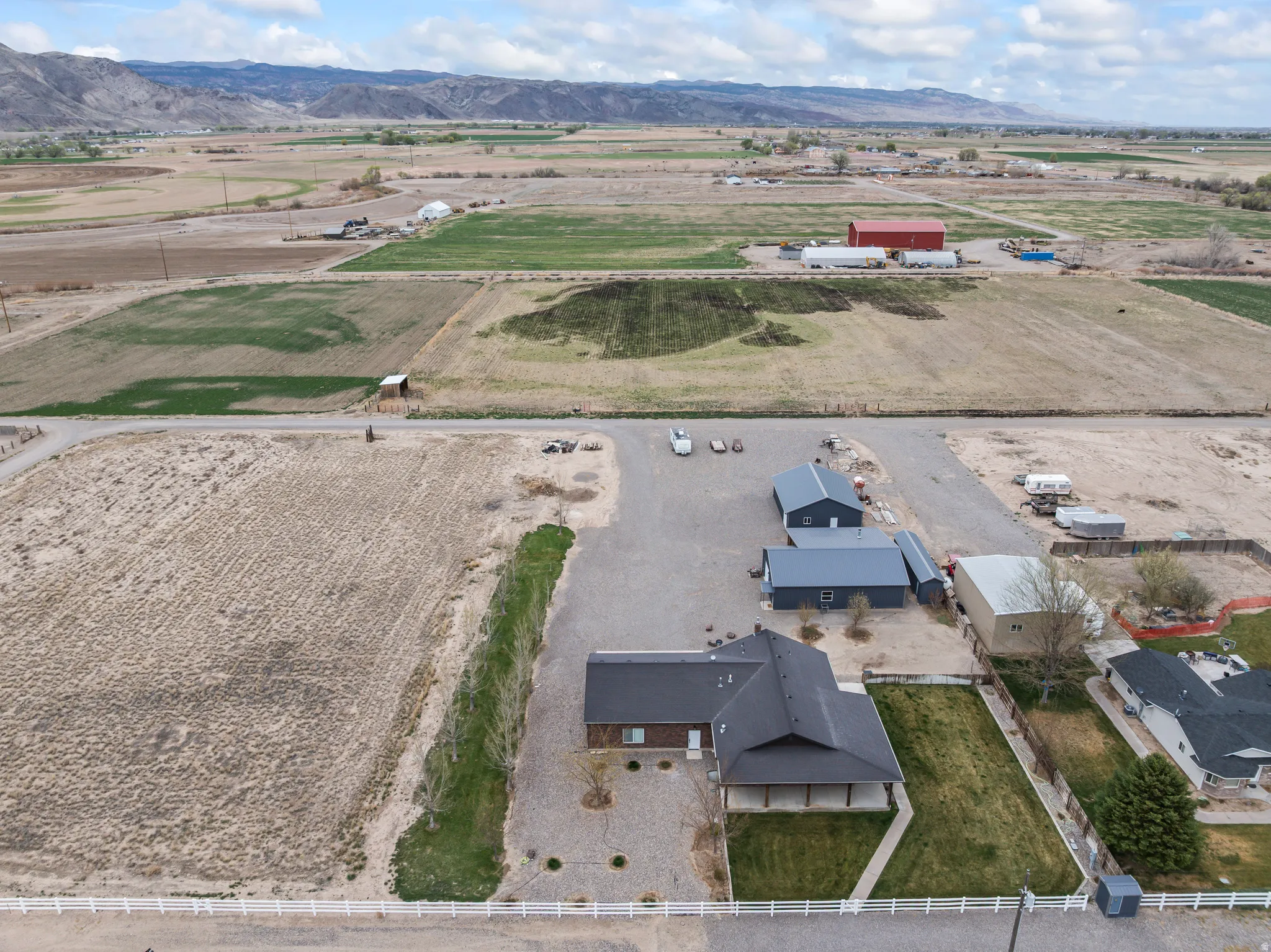 Aerial perspective showcasing the property with a dark-roofed residence, extensive gravel parking, and a manicured lawn area