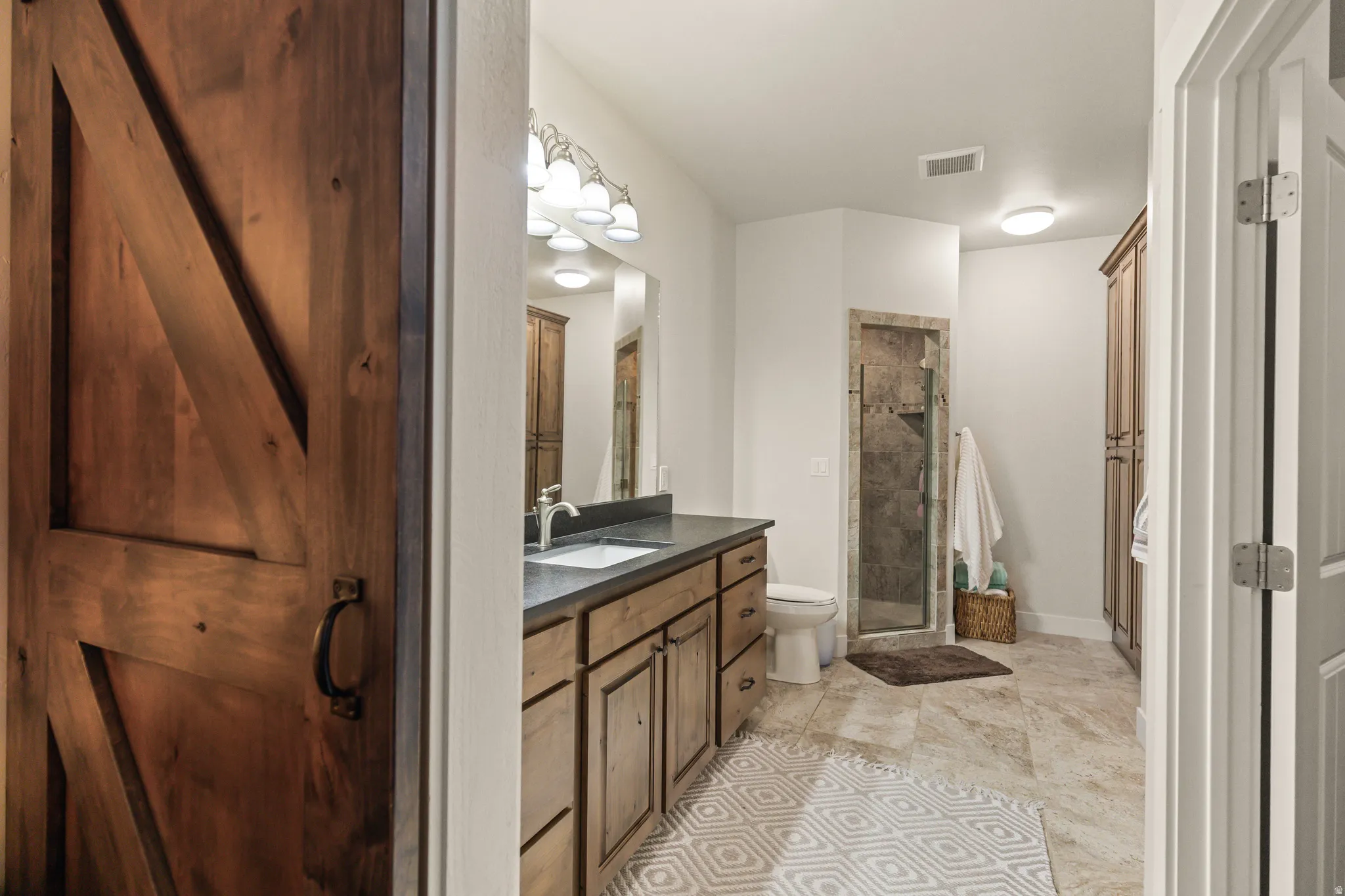 Barn door entry into a bathroom featuring a wood-finish vanity with a dark countertop and undermount sink
