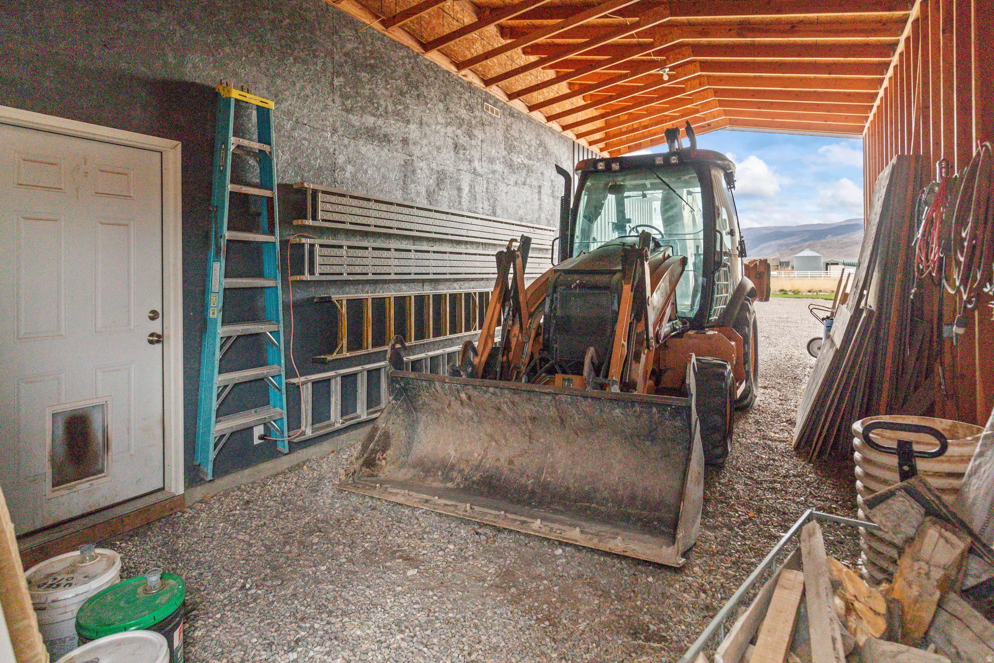 Covered outdoor storage area featuring exposed wood beam ceiling, gravel flooring, and durable panel walls