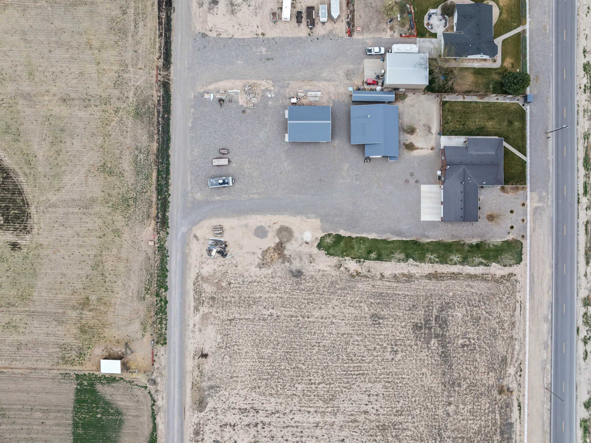 Aerial perspective showcasing multiple structures on a gravel lot, featuring three distinct buildings with dark gray roofing