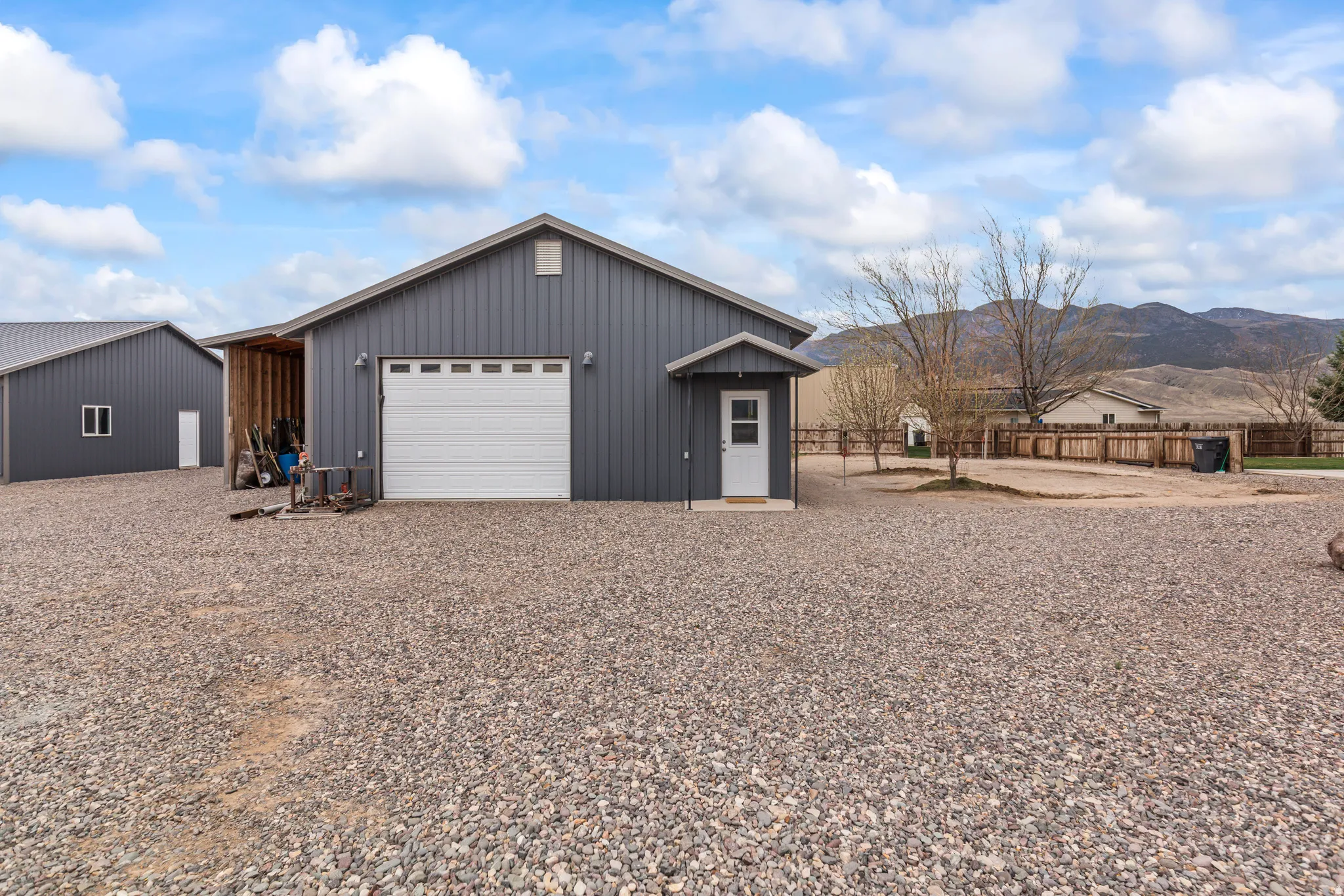 Detached garage structure featuring a roll-up garage door, a covered entry door, and dark gray corrugated metal siding