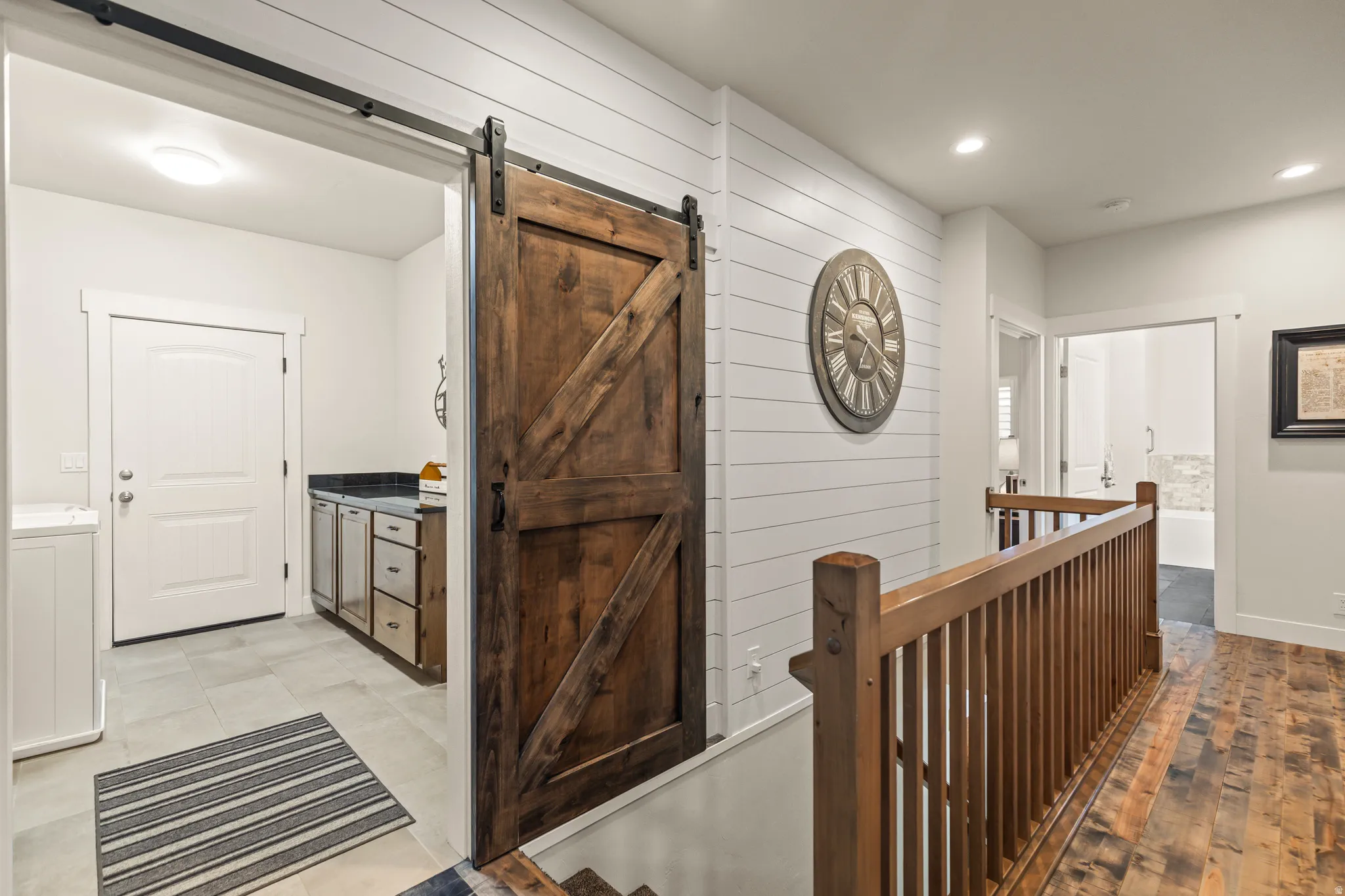 Wood-finish flooring and a wood balustrade frame a hallway with shiplap wall detailing