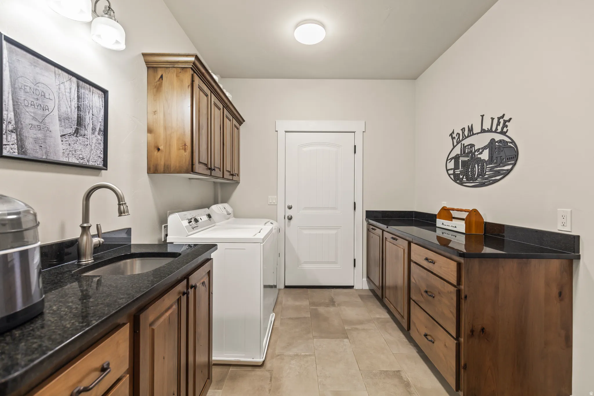 Functional utility room featuring wood-finish cabinetry, dark stone countertops, an undermount sink with a gooseneck faucet, and tile flooring