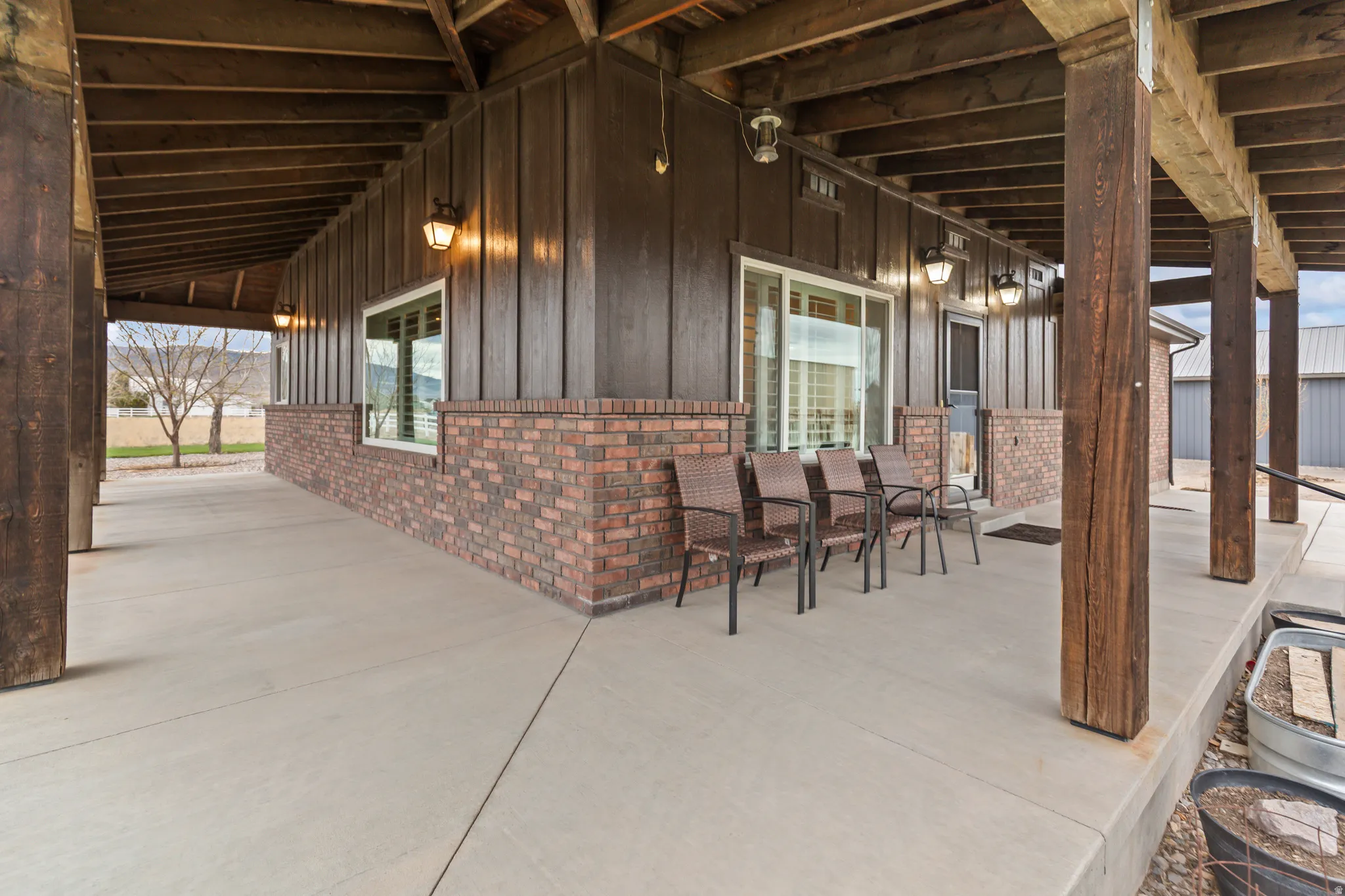 Expansive covered patio featuring a concrete floor, exposed wood beams, wood-plank siding, a brick facade, and multiple windows