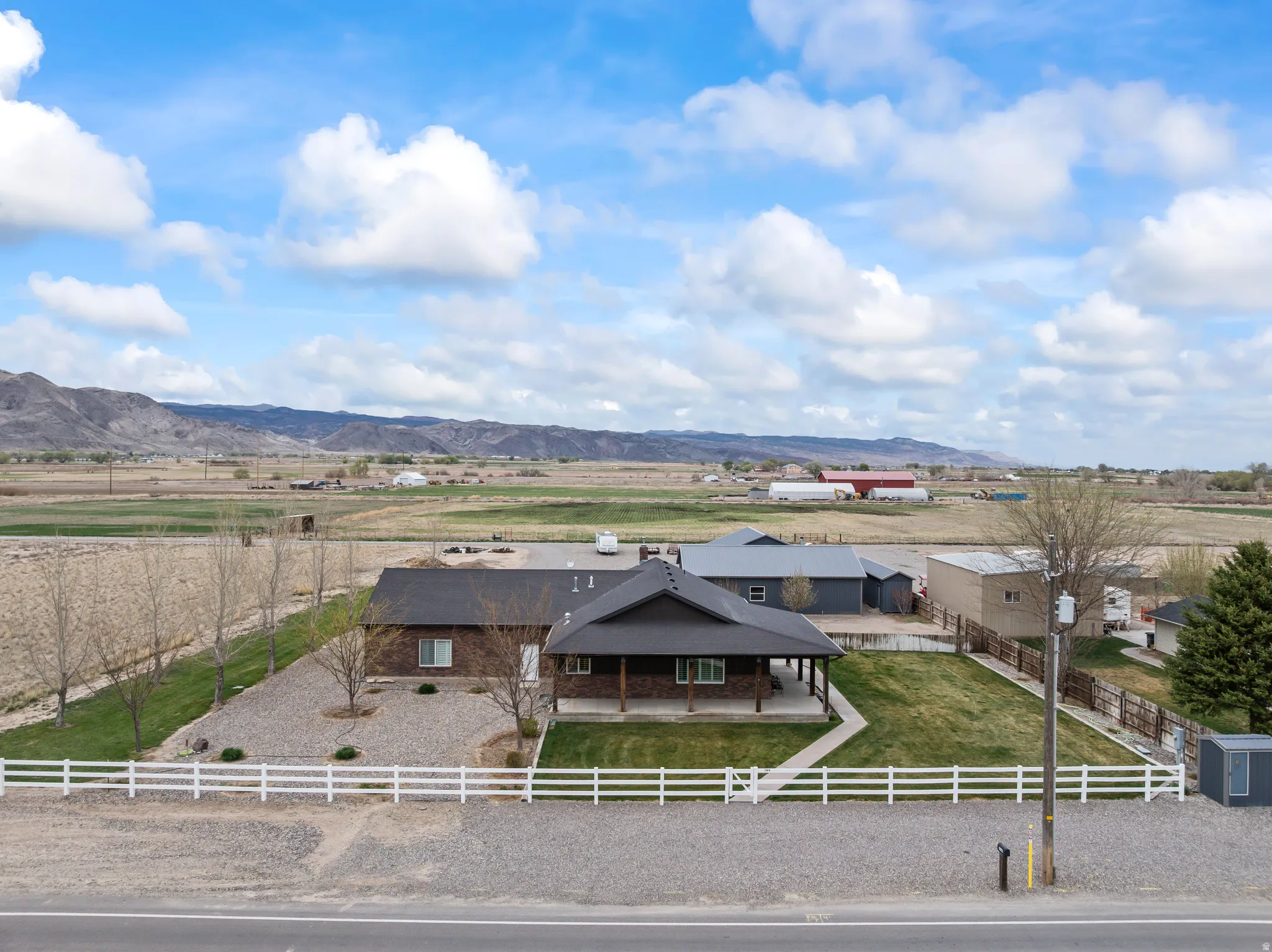 Ranch-style residence featuring a covered front porch, a white picket fence, and an expansive gravel driveway